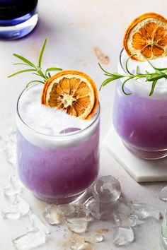 two glasses filled with purple liquid and garnished with orange slices