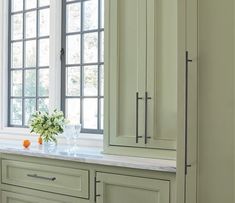 a vase with flowers sitting on top of a kitchen counter next to two large windows