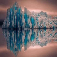 an iceberg is reflected in the water on a calm day with no one around it