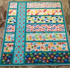 a quilted table runner made with colorful strips and fish on the border, sitting on top of a floral fabric