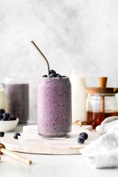 a blueberry smoothie in a glass with a straw and some berries on the side