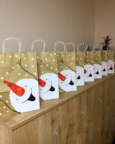 paper bags with snowmen painted on them are lined up on a wooden table in front of a wall