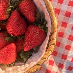 a basket filled with lots of ripe strawberries on top of a checkered table cloth