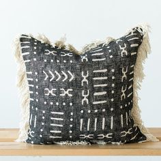 a black and white pillow with fringes on top of a wooden table next to a wall