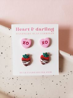 two pairs of heart and arrow earrings on top of a white plate with pink background