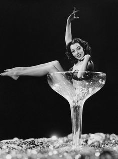 a woman sitting in a martini glass with her legs spread out and one leg on the rim