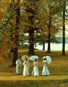 four women in white dresses are standing near trees