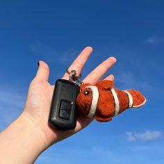 a hand holding a small keychain with a clown fish on it's thumb