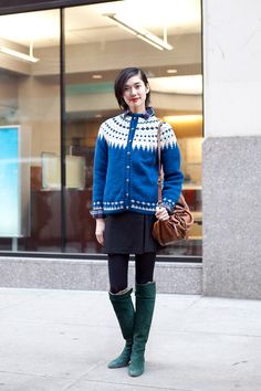 a woman standing in front of a building wearing green boots and a blue cardigan sweater