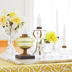 a table topped with glass vases filled with yellow flowers next to candlesticks