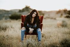 a woman sitting on top of a red chair in a field