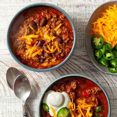 three bowls filled with chili, cheese and green peppers on top of a wooden table