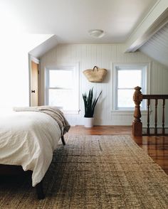 a bedroom with white walls, wooden floors and an area rug that has a plant on it