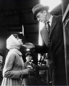 a man in a suit and tie is handing something to a woman wearing a hat