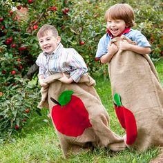 two young boys are playing in an apple orchard with their large sacks full of apples