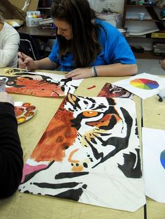 two women sitting at a table working on paintings