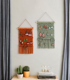 two wall hangings on the side of a white wall next to a cactus and potted plant