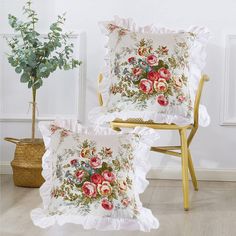 two pillows with flowers on them sitting next to a chair and potted plant in the corner