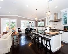 a large open concept kitchen and living room with hardwood floors, white cabinets, black counter tops, and bar stools