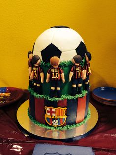 a soccer themed cake with figurines around it on a table in front of a yellow wall