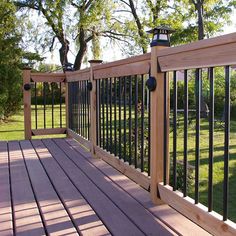 a wooden deck with black iron railings in the middle of a grassy area next to trees