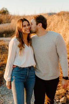 a man and woman standing next to each other in front of some tall grass with the sun shining on them