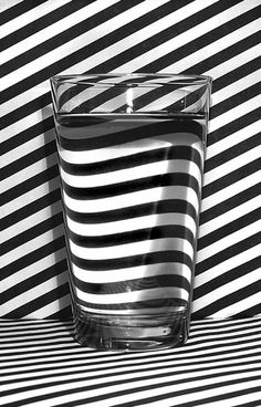 a black and white photo of a glass with water in it on a striped surface