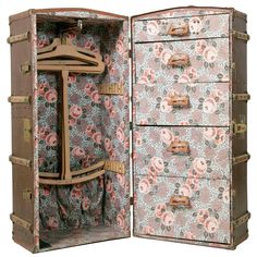 an open suitcase with flowers on it and clothes hangers in the door, as well as two drawers