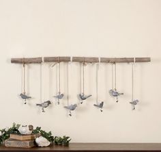 several birds hanging from a wooden branch on a wall next to a book and vase