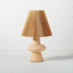 a table lamp with a beige shade on the base and a white wall in the background