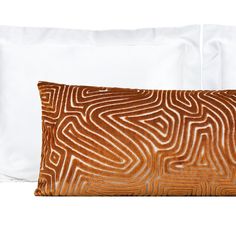 two pillows on top of each other in front of a white pillow case with an orange and brown pattern