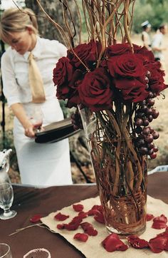 a vase filled with red roses sitting on top of a table next to wine glasses