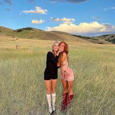 two women standing in tall grass posing for the camera with their arms around each other