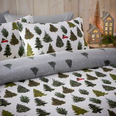 a bed with christmas trees on it in front of a wooden wall and small house