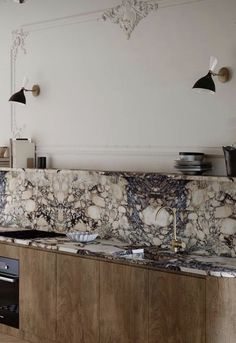 a kitchen with marble counter tops and wooden cabinets in the center, along with two black pendant lights