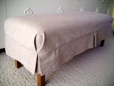 an upholstered footstool on carpeted area with white walls and flooring