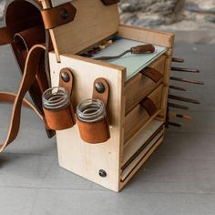 a wooden box with two mason jars in it and leather straps hanging from the front