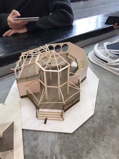 a model of a building on top of a white piece of paper next to a person holding a cell phone