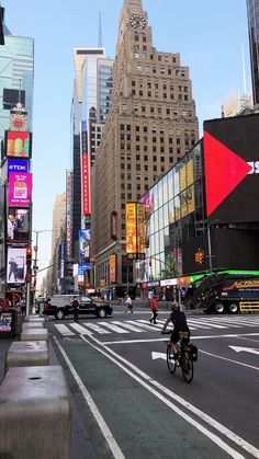 a man riding a bike down a street in the middle of a city with tall buildings