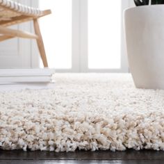 a white area rug on the floor with a chair and potted plant in the background