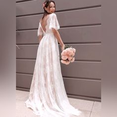 a woman in a white dress holding a bouquet and standing next to a gray wall