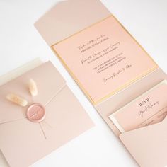 the wedding stationery is set on top of pink envelopes, with a white feather sticking out of it