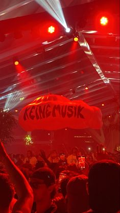 a large group of people in a room with red lights and some signs on the ceiling