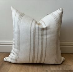 a white and brown striped pillow sitting on top of a wooden floor next to a wall