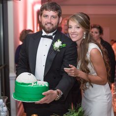 a man and woman standing next to each other in front of a cake on a table