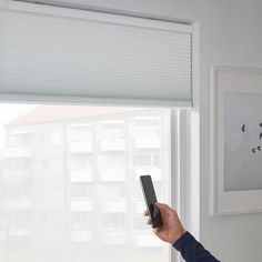 a person holding a remote control in their hand near a window with blinds on it