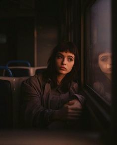 a woman sitting on a bus looking out the window at another person behind her in the dark