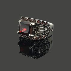 a black and red stone ring on top of a reflective surface with the reflection of it