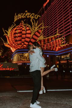 a man and woman are kissing in front of a building with neon lights on it