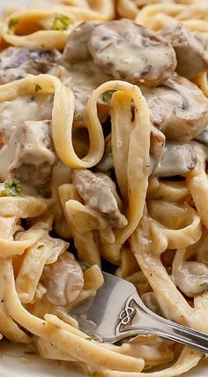 a white plate topped with pasta covered in sauce and mushrooms next to a silver fork